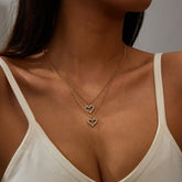 Two gold heart pendants adorned with diamonds, featuring a layered design in 18K gold-plated and cubic zirconia.