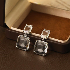 Stunning clear crystal earrings in a square drop design, set in silver-plated metal for a chic and modern look.