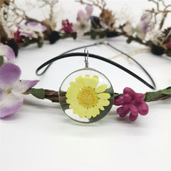 Yellow daisy displayed in a white glass pendant, elegantly hanging from a round cord necklace.