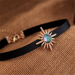 A black choker featuring a sunburst stone, crafted with crystal and cubic zirconia, and 18k gold-plated accents.