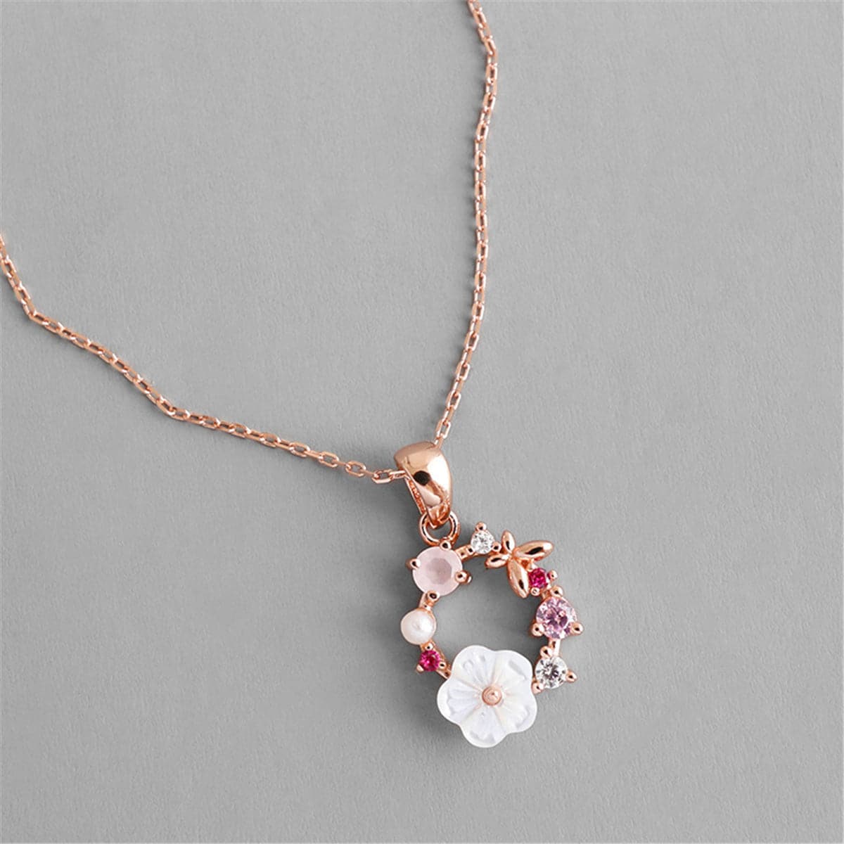 Rose gold necklace featuring pink flowers and white stones, adorned with cubic zirconia and a pearl pendant.