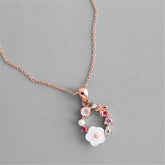 Rose gold necklace featuring pink flowers and white stones, adorned with cubic zirconia and a pearl pendant.