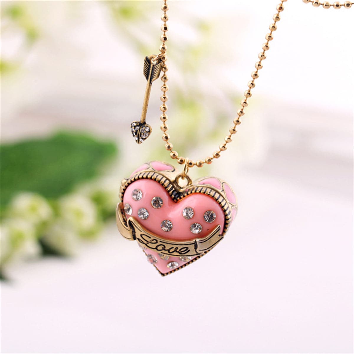 Pink heart-shaped pendant with a diamond arrow, featuring a cubic zirconia and 18K gold-plated 'Love' locket design.