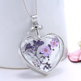 Heart-shaped silver pendant necklace featuring pressed purple peach blossoms encased in resin. A delicate floral accessory.