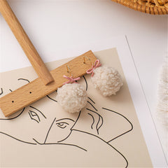 Stunning 18K gold-plated earrings adorned with fluffy white pom poms and a playful pink bow for a trendy look.