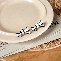 Two bow-shaped earrings in black and white, made from white polyurethane and adorned with silver plating.