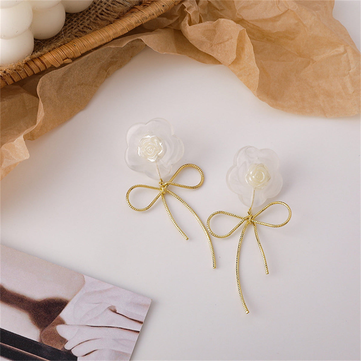 White resin flower and gold-plated bow drop earrings showcases their elegant design.