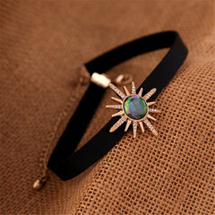 Chic black choker showcasing a sunburst stone, embellished with crystal and cubic zirconia, and 18k gold plating.