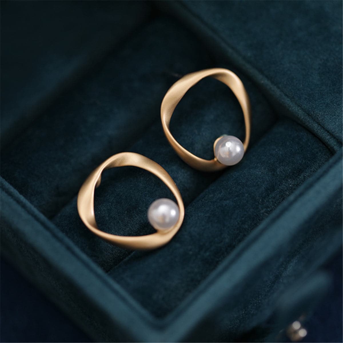 Two gold-plated earrings featuring a central pearl, designed as open twist round stud earrings.