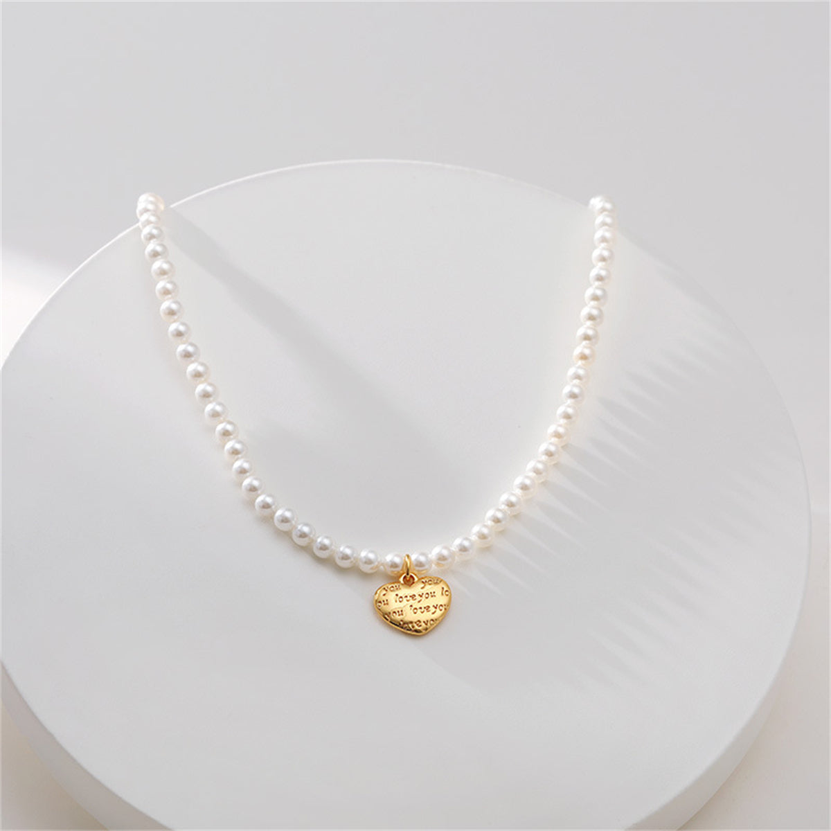A gold heart charm on a white pearl necklace, featuring an 18K gold-plated 'Love You' pendant.