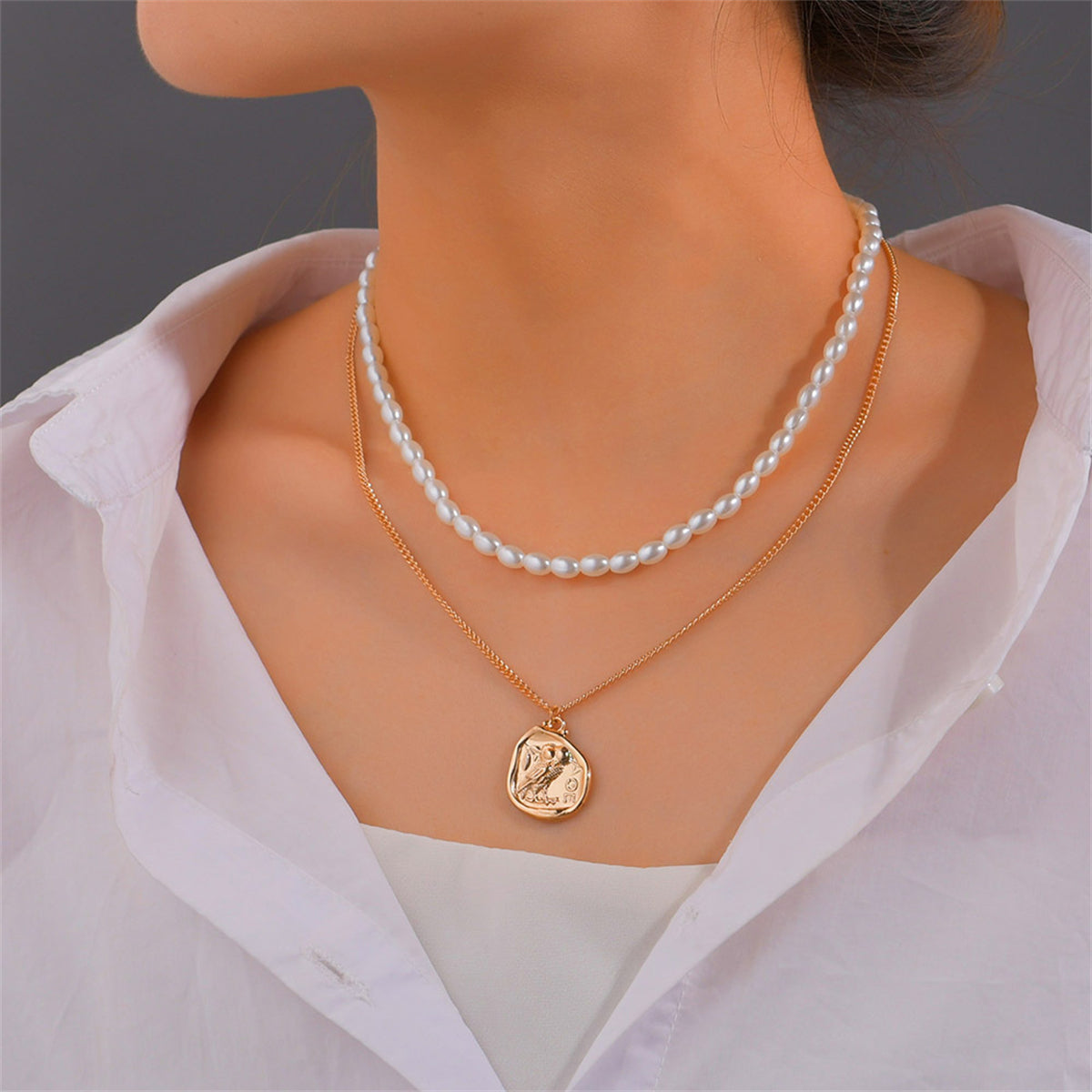 A layered necklace featuring an 18K gold-plated owl pendant, adorned with a coin charm and a pearl chain.