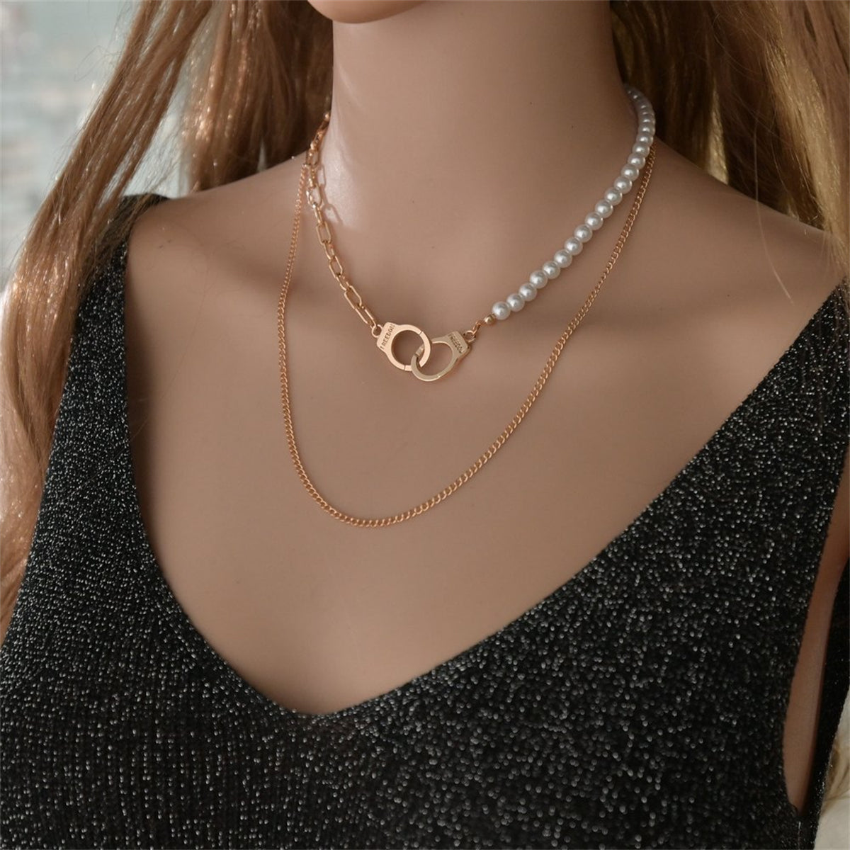 A gold chain and a pearl necklace layered together, showcasing an elegant 18K gold-plated handcuff pendant.