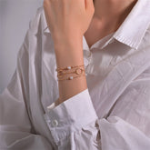 A layered bracelet featuring a gold chain adorned with pearls and a circular charm, elegantly designed in 18K gold plating.