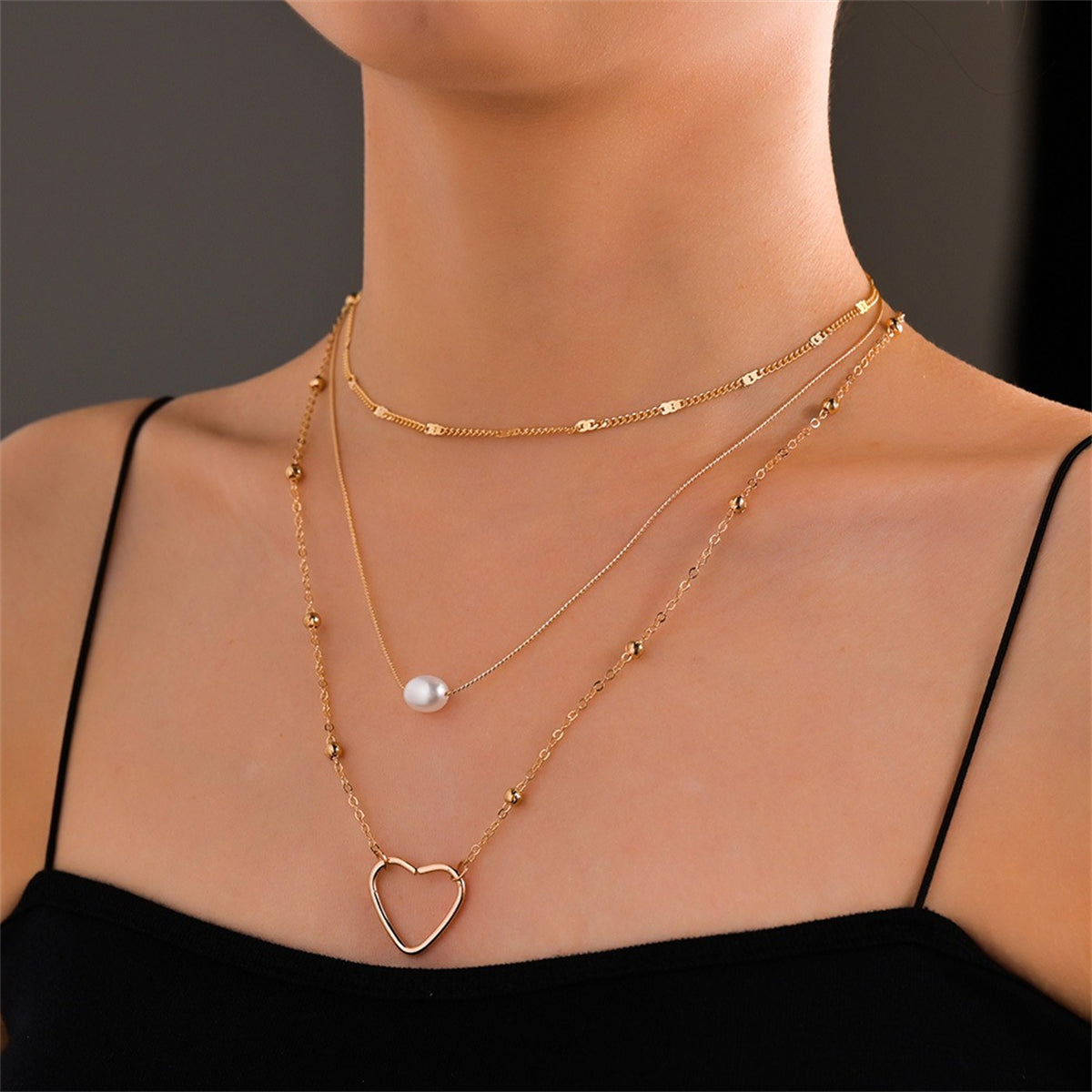 A layered pendant necklace featuring an 18K gold-plated heart and a pearl, elegantly designed for a sophisticated look.