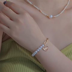 A delicate bracelet made of white pearls, complemented by a gold heart charm, embodying elegance and affection.