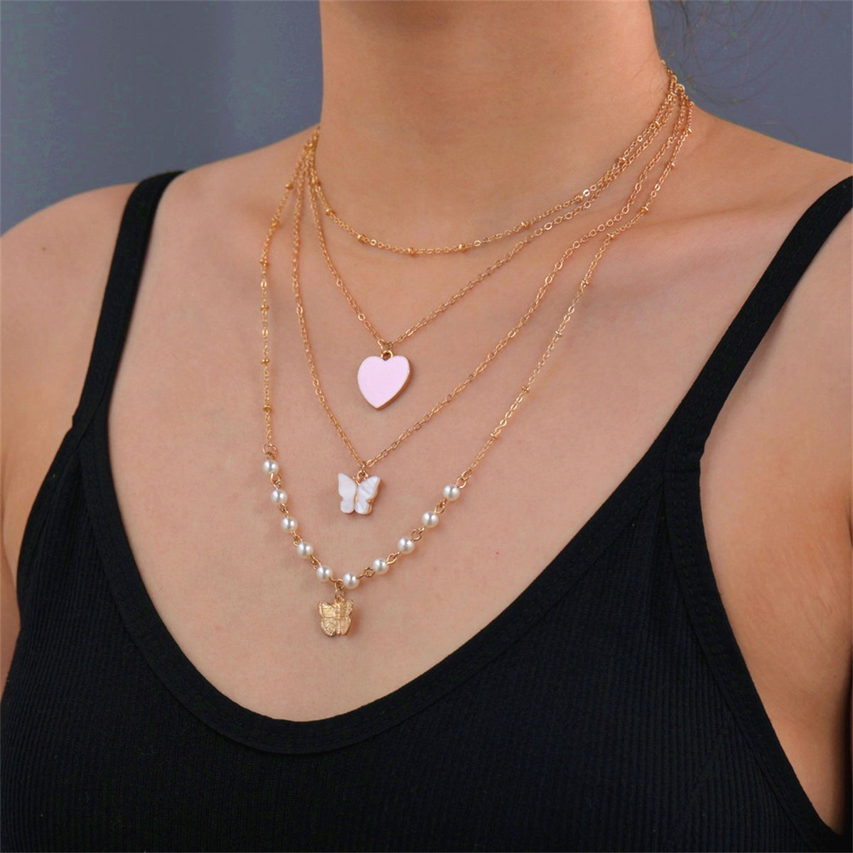 A pink heart necklace featuring a butterfly charm, adorned with pearls and crafted in 18K gold plating.