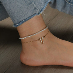 A pair of stylish anklets adorned with pearls and gold chains, highlighting a pearl and 18K gold-plated shell charm.