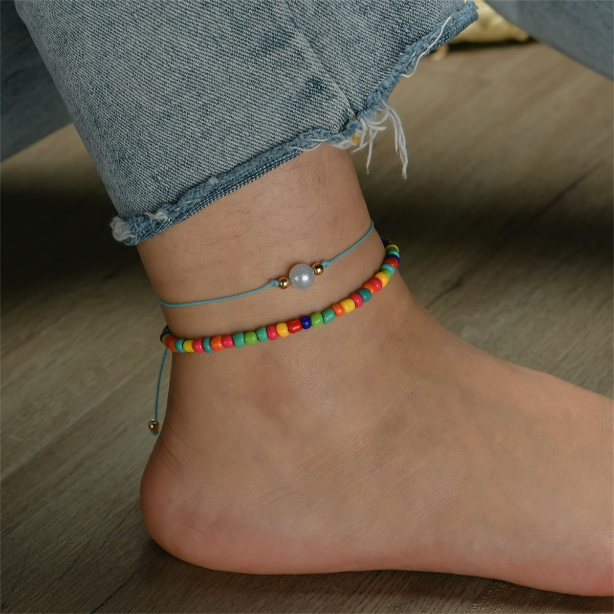 A pair of anklets adorned with rainbow beads and a blue cord, included in the Red Multicolor Howlite Stretch Anklet Set.