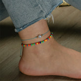 A pair of anklets adorned with rainbow beads and a blue cord, included in the Red Multicolor Howlite Stretch Anklet Set.
