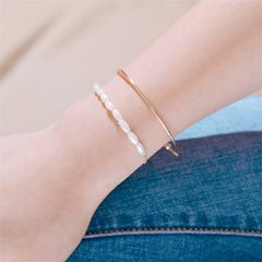Elegant gold bangles featuring pearls and a chain, part of the Pearl & 18K Gold-Plated Oval Bracelet Set.