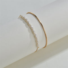 A pair of gold bangles embellished with pearls and a chain, representing the Pearl & 18K Gold-Plated Oval Bracelet Set.