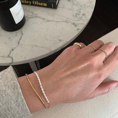 Gold bangles with pearls and a chain, elegantly designed as part of the Pearl & 18K Gold-Plated Oval Bracelet Set.