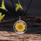 Close-up of a yellow daisy in a white glass pendant, part of a round cord necklace design.