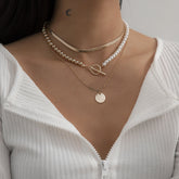 Layered necklace featuring a pearl and an 18K gold-plated coin, elegantly styled for a chic look.