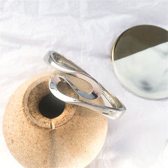 A silver bracelet with a unique curved design, this silver-plated ribbon bangle exudes elegance and contemporary style.