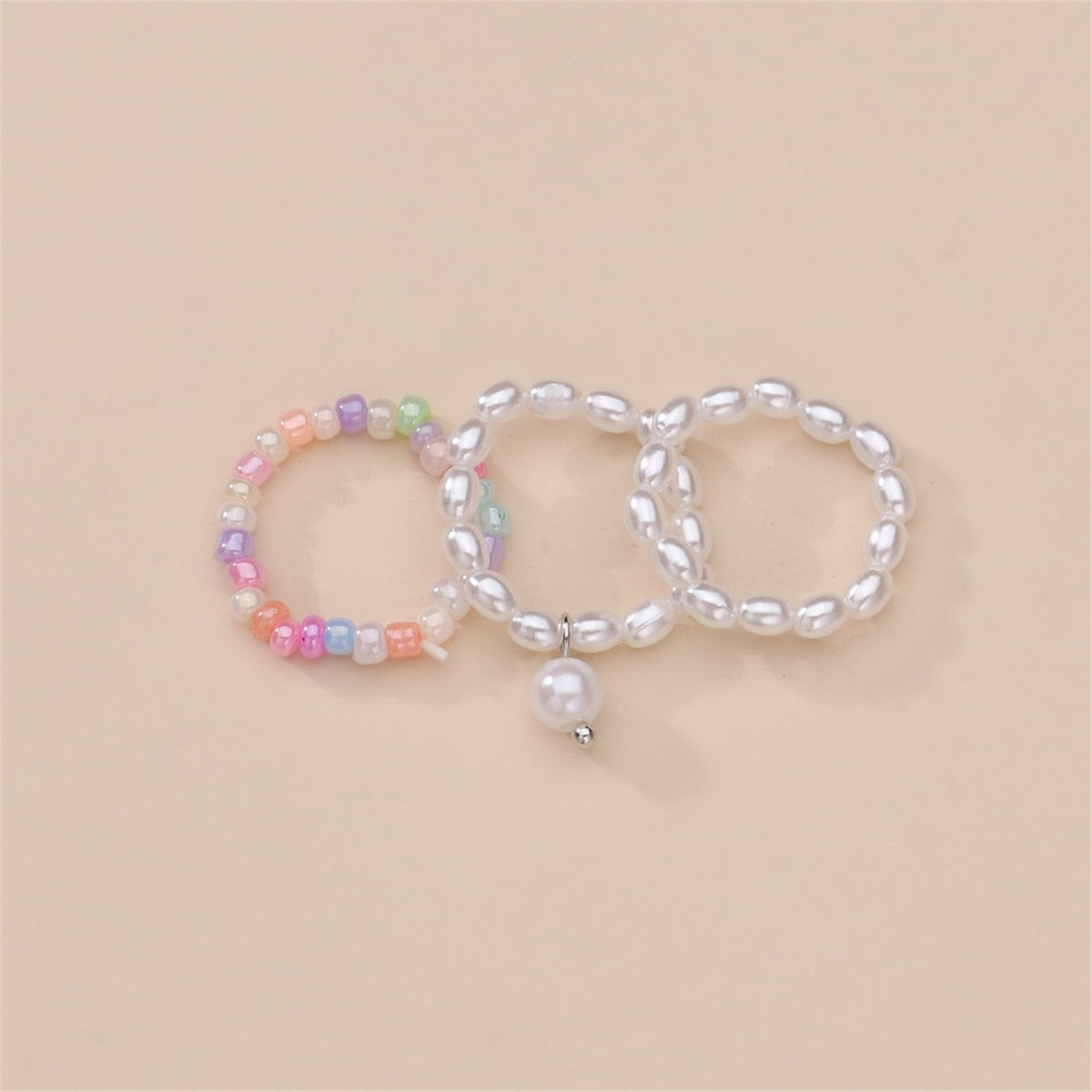 Three distinct rings showcasing pearls and a pearl charm, crafted as a stylish beaded stretch ring set.