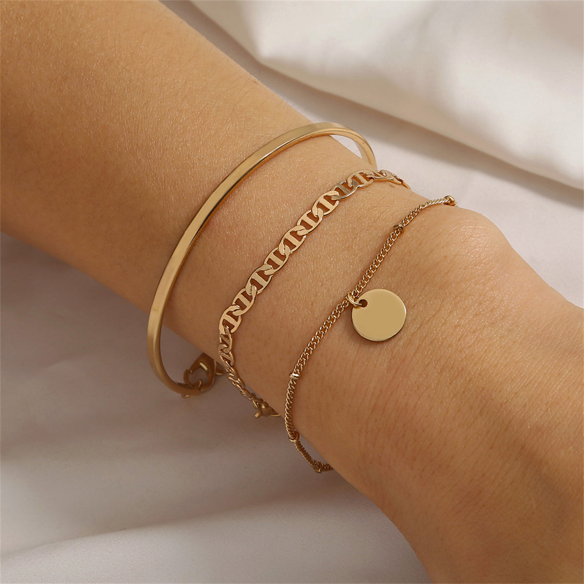Three elegant gold bracelets featuring a stylish disc charm, perfect for adding a touch of luxury to any outfit.