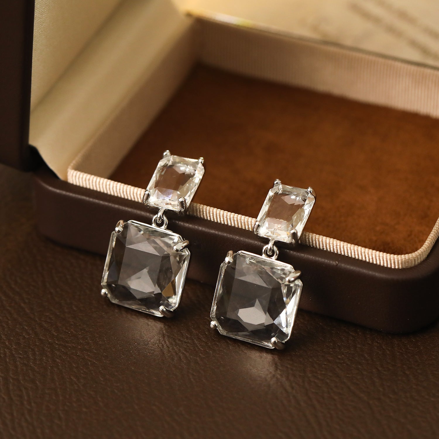 Stunning clear crystal earrings in a square drop design, set in silver-plated metal for a chic and modern look.