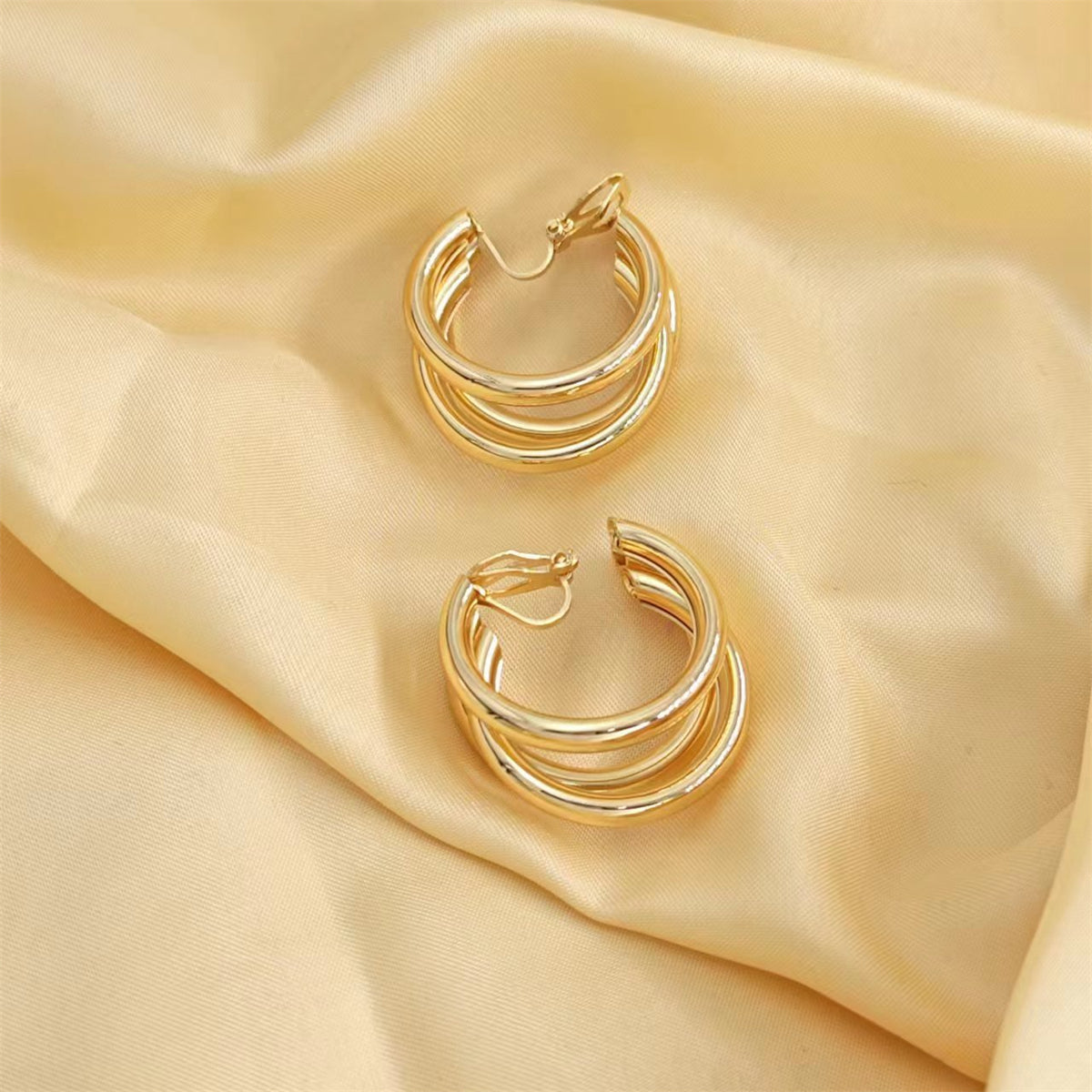 Beautiful 18K gold-plated crisscross hoop earrings on silky fabric, emphasizing their luxurious appeal and intricate design.