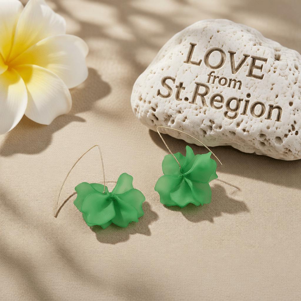 Green flower-shaped dangle earrings displayed on a beige surface next to a white and yellow flower and a decorative stone engraved with 'LOVE from St.Region'.