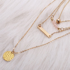 Three stylish layered necklaces with gold-plated charms, including a striking 18K gold-plated bar and beaded pendant.