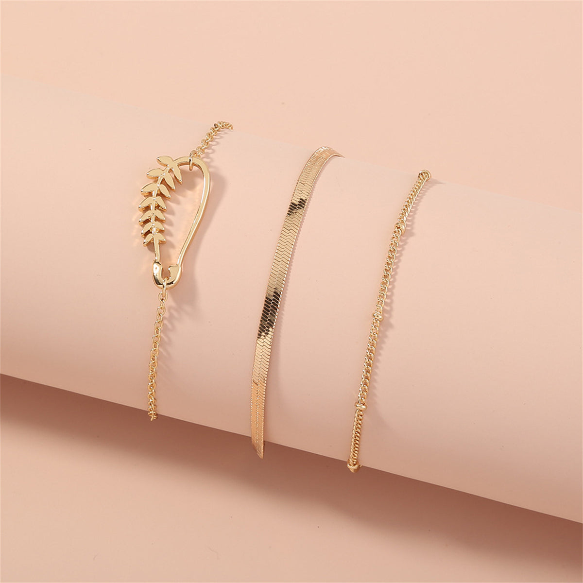 A stunning set of three gold bracelets with a delicate chain and leaf charm, showcasing 18K gold-plated craftsmanship.