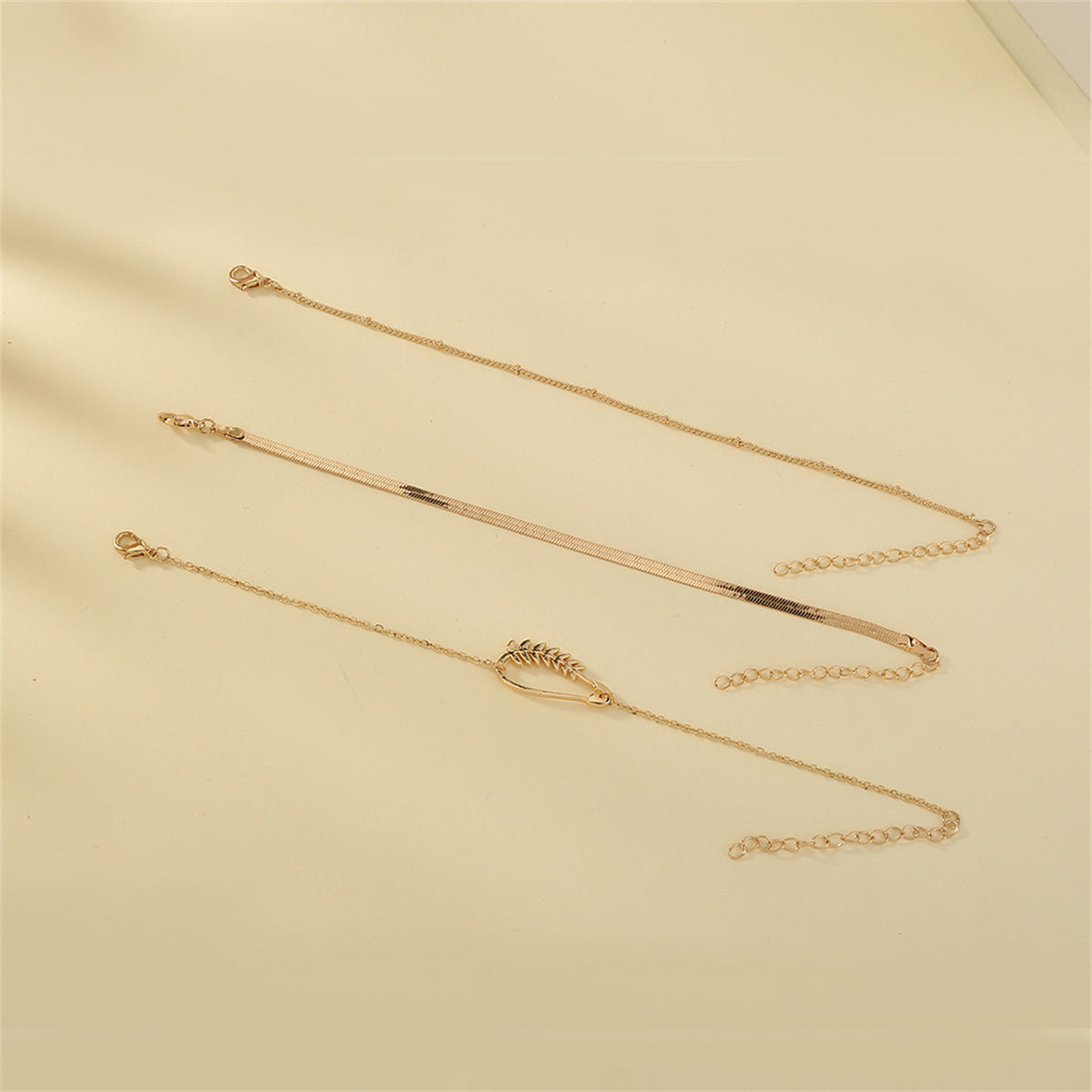Three exquisite gold bracelets with a chain and leaf charm, beautifully designed in 18K gold plating for a luxurious touch.