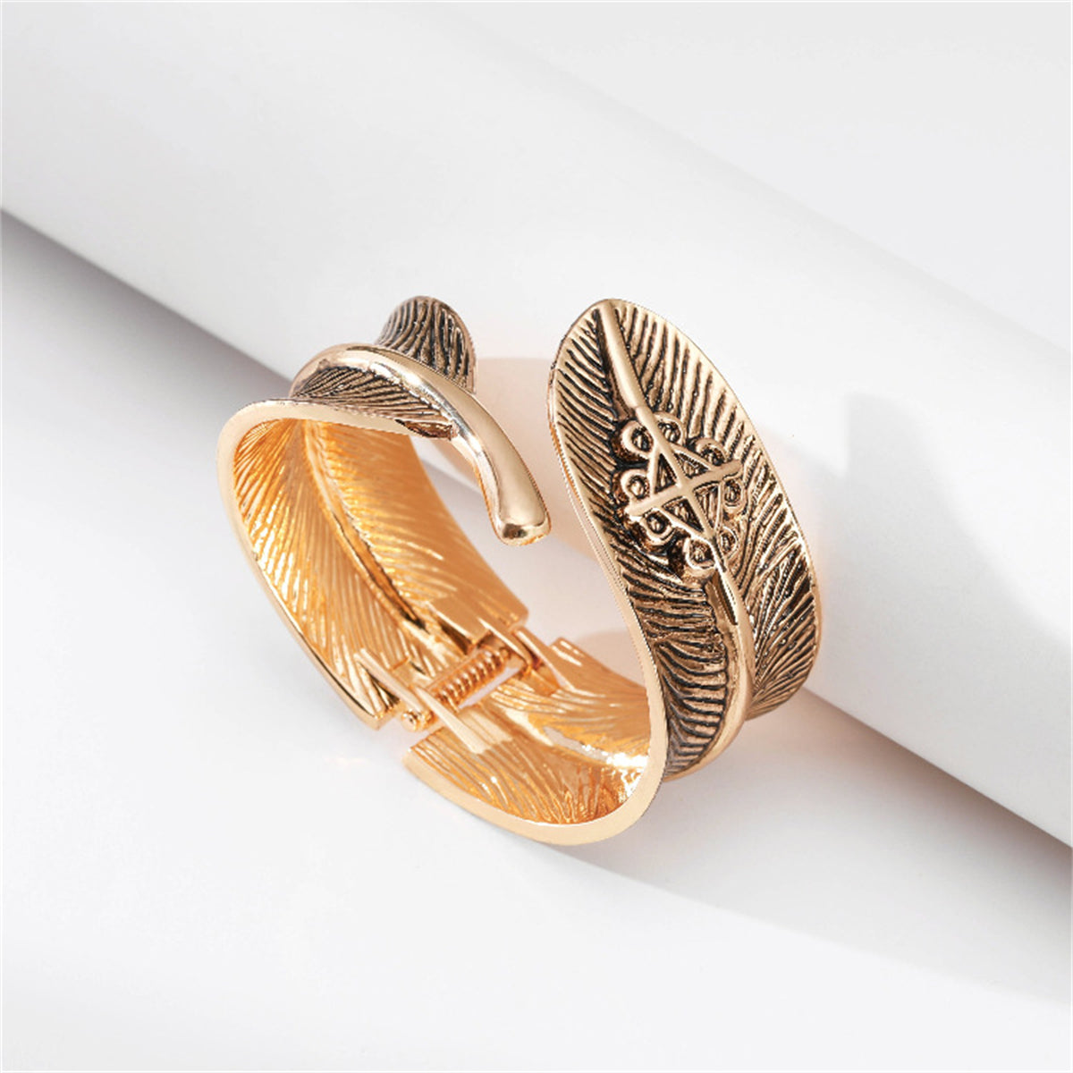 An 18K gold-plated cuff adorned with a delicate feather design, made from enamel, exemplifying a stylish bypass bangle.