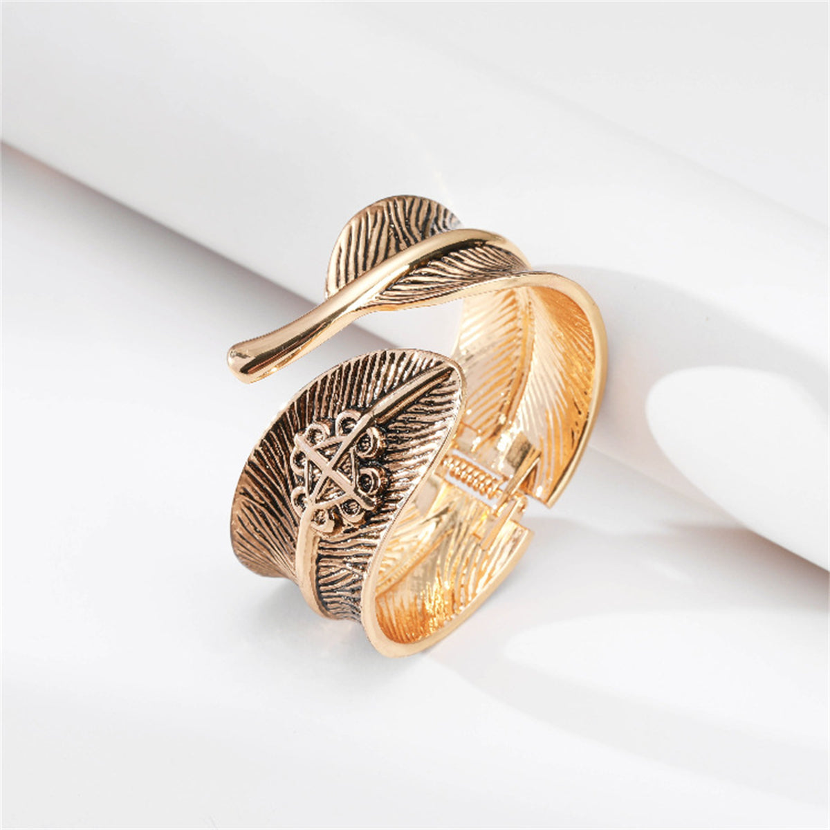 A gold-plated cuff with a feather design, crafted in enamel, presenting a sophisticated bypass bangle style.
