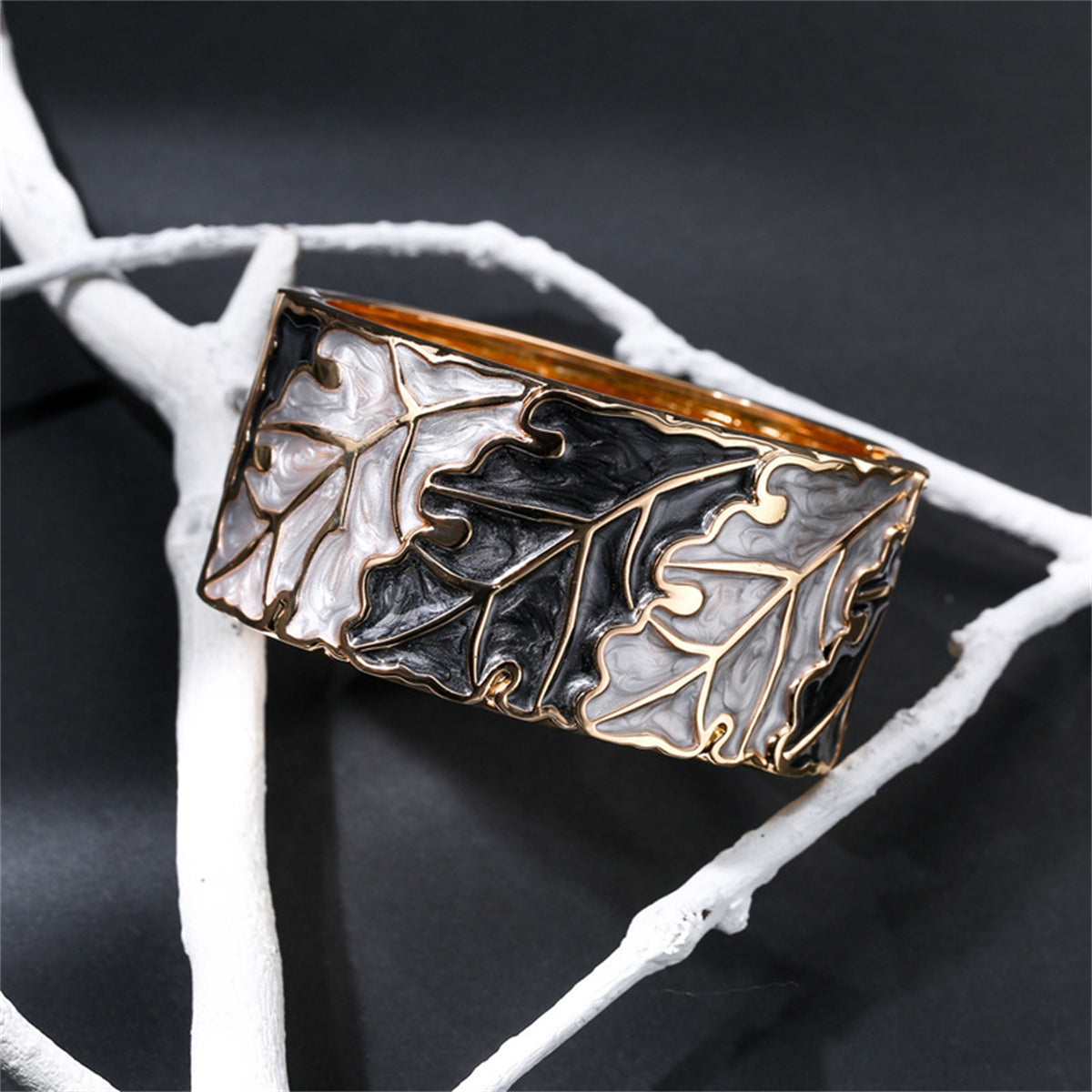 A stylish bangle adorned with oak leaves, showcasing gold and silver accents, made from gray and black enamel with 18K gold.
