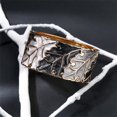 A stylish bangle adorned with oak leaves, showcasing gold and silver accents, made from gray and black enamel with 18K gold.