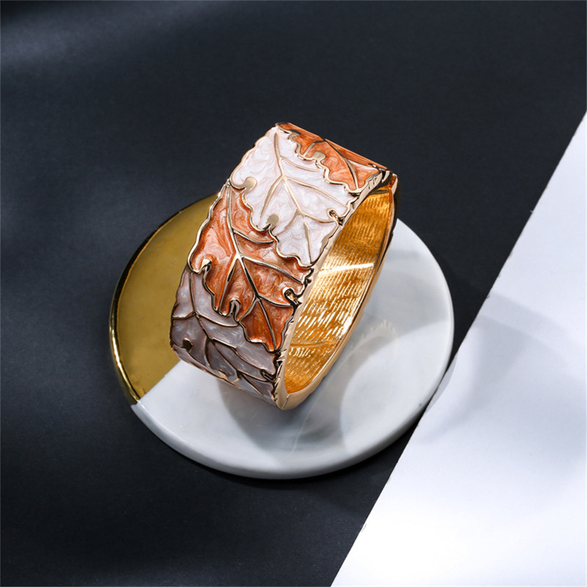 A refined bangle in gold and white, featuring a delicate leaf design, accented with orange enamel and 18K gold plating.