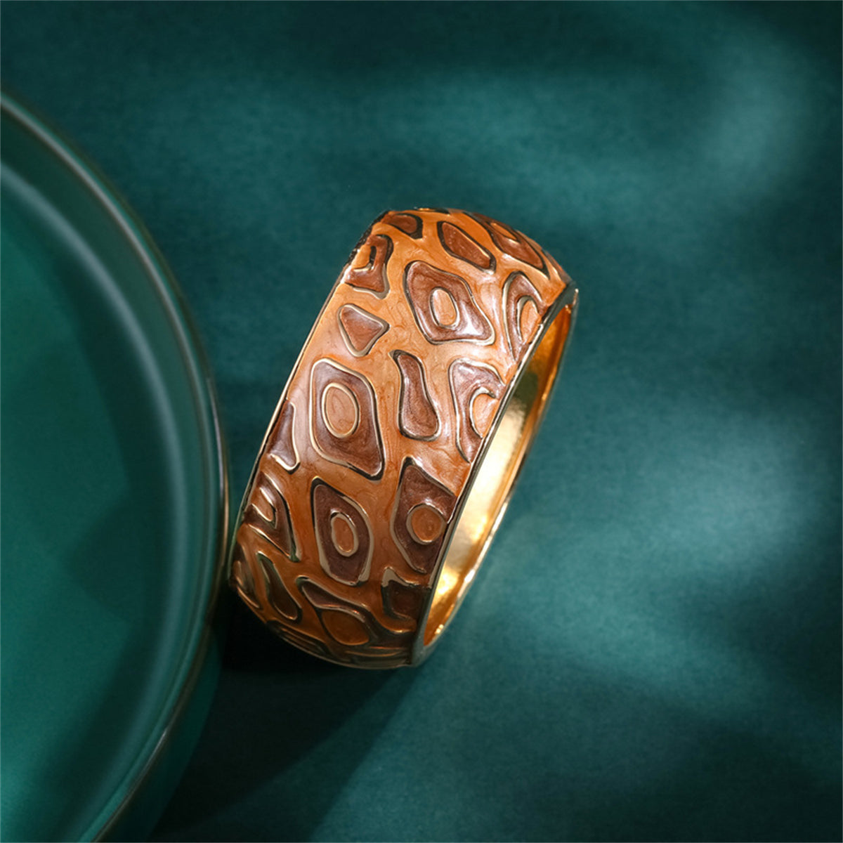 A sophisticated gold and brown bangle adorned with a patterned design, featuring brown enamel and 18K gold plating.