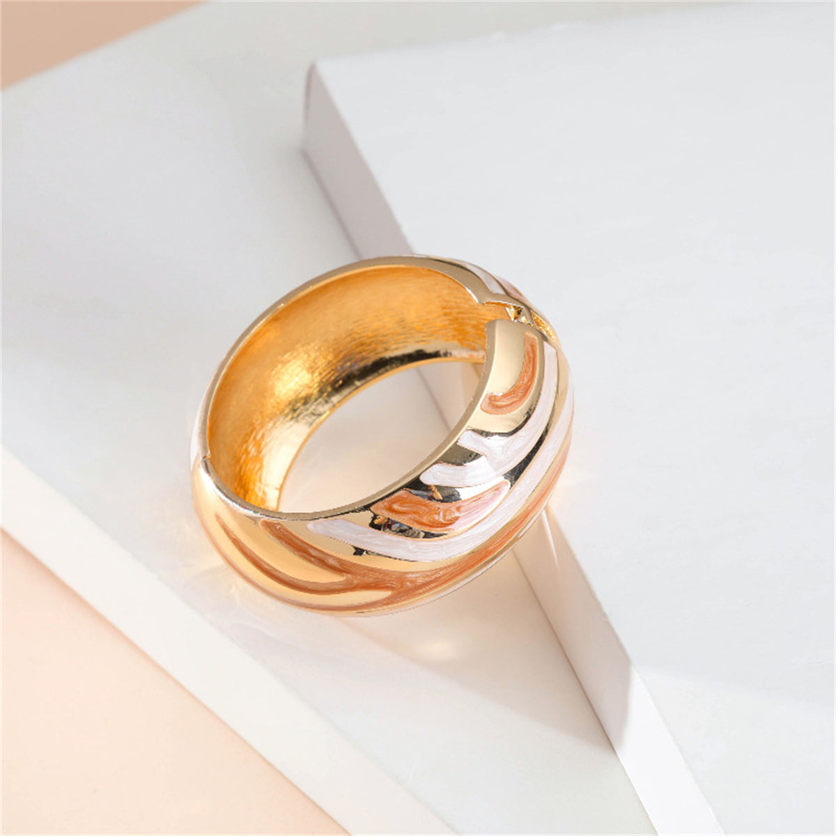 A chic gold and orange bangle with a swirl design, composed of orange enamel and finished with 18K gold plating.