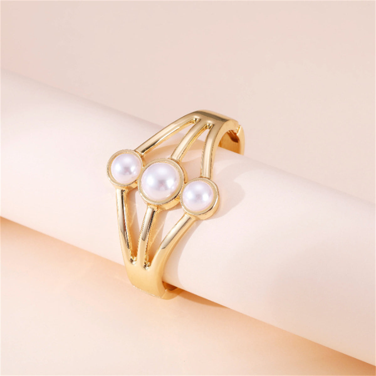 A luxurious gold-plated bangle adorned with three pristine white pearls, showcasing a sophisticated layered bangle style.