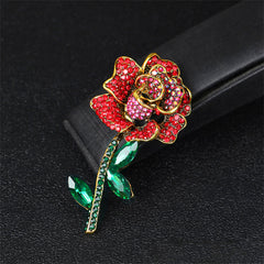 Elegant 18K gold-plated rose brooch embellished with red cubic zirconia and green stones, showcasing exquisite craftsmanship.