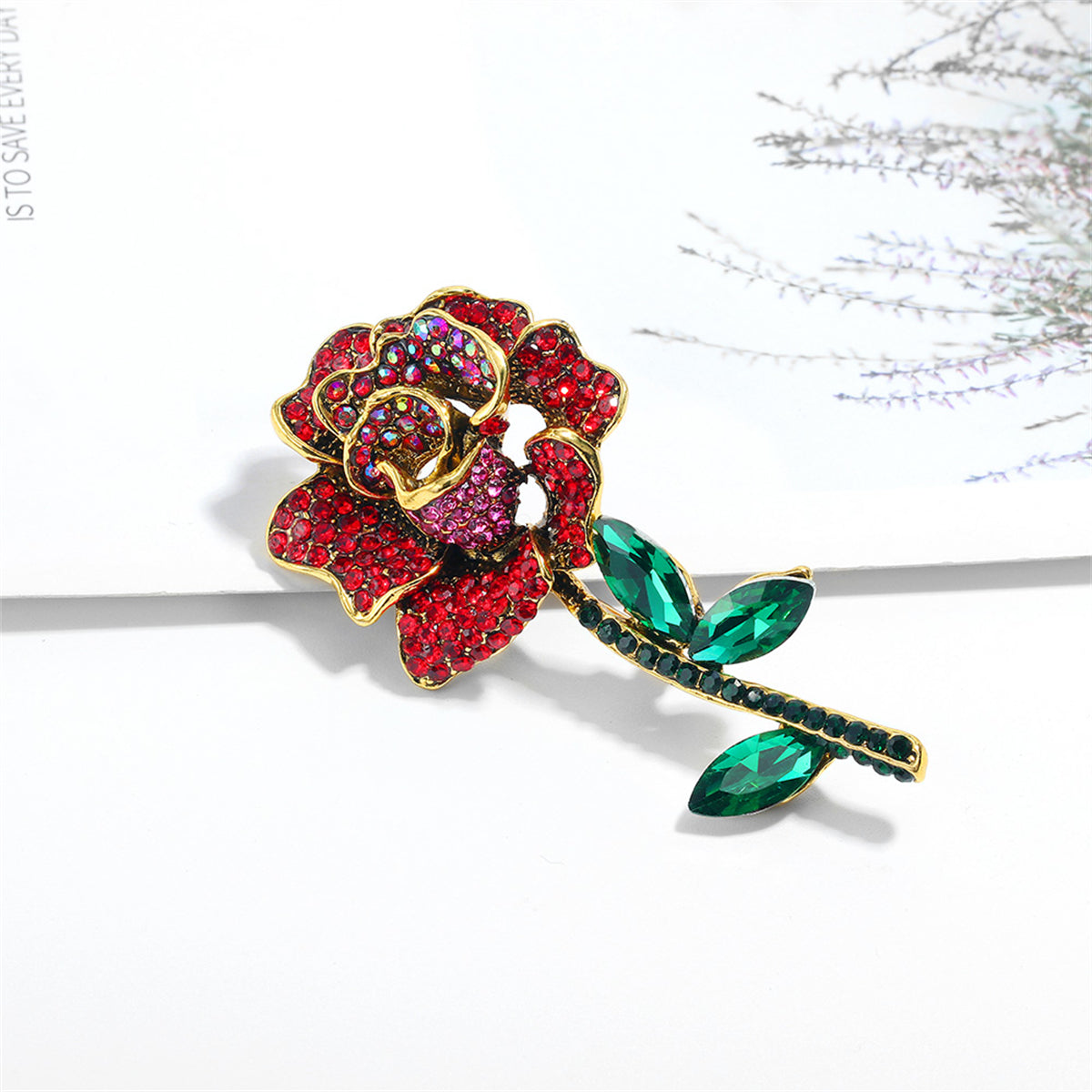 A luxurious red rose brooch in 18K gold plating, adorned with red cubic zirconia and green crystals, perfect for any occasion.