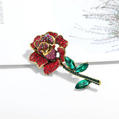A luxurious red rose brooch in 18K gold plating, adorned with red cubic zirconia and green crystals, perfect for any occasion.