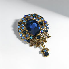 A decorative blue and gold brooch with a large oval stone, enhanced by cubic zirconia in an elegant flower drop motif.