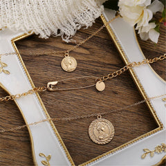 Beautifully layered gold necklaces with a coin and safety pin pendant, perfect for elevating your fashion game effortlessly.